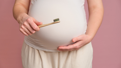 Pregnant woman holding a toothbrush, studio pink background. Concept of pregnancy and brushing teeth